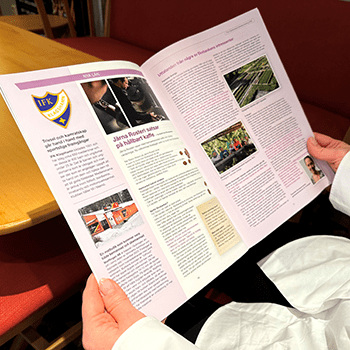 Någon håller upp ett uppslag av senaste Goda Affärer-tidningen, nr 2026